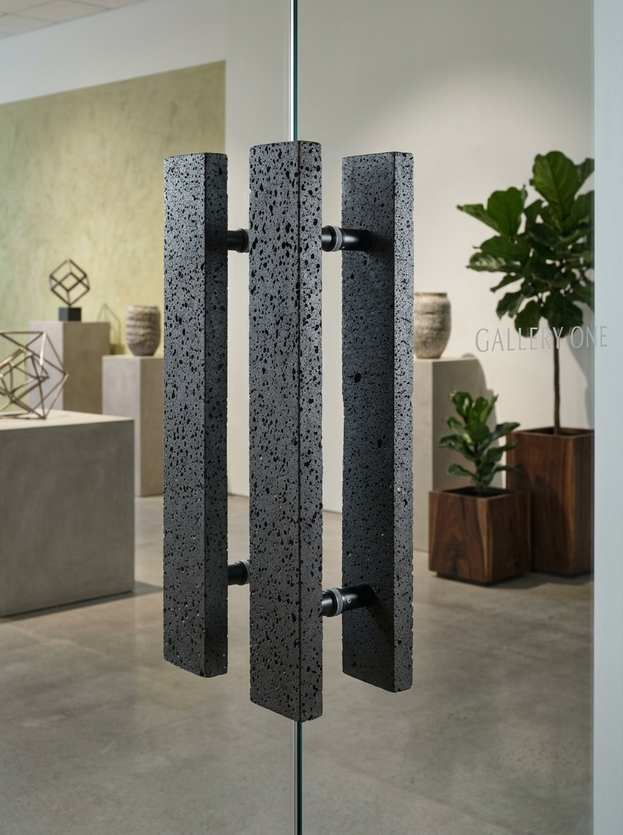 Black basalt bar stone door pull with porous volcanic texture mounted back-to-back on an office glass partition