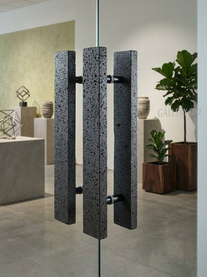 Black basalt bar stone door pull with porous volcanic texture mounted back-to-back on an office glass partition